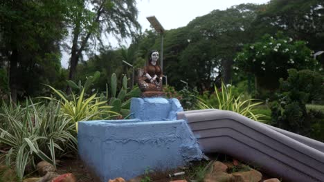 una pequeña estatua en un jardín exuberante rodeado de vegetación y un pedestal azul pintado
