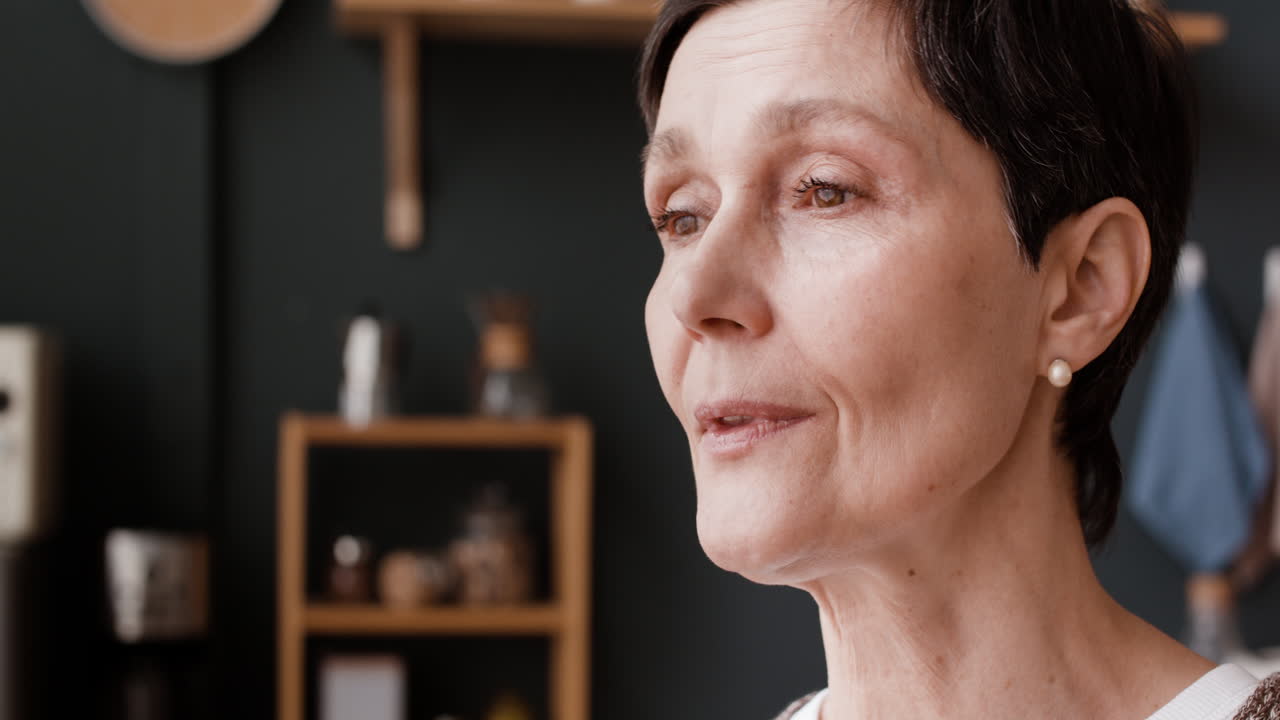 A mature woman drinking a beverage in her kitchen
