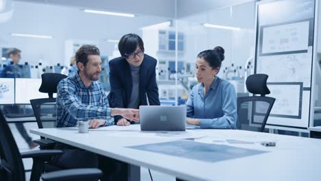 modern factory office meeting: female project manager, asian branch supervisor talk with chief product engineer who shows them laptop screen. team of professionals solving technological problems