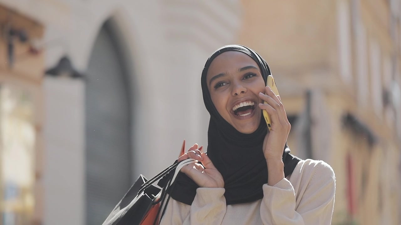 Giovane donna felice con hijab che parla al telefono mentre fa acquisti