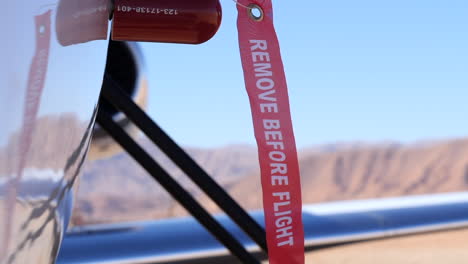 a "remove before flight" tag attached to an aircraft slowly blowing in the wind, high mountains in soft focus slomo