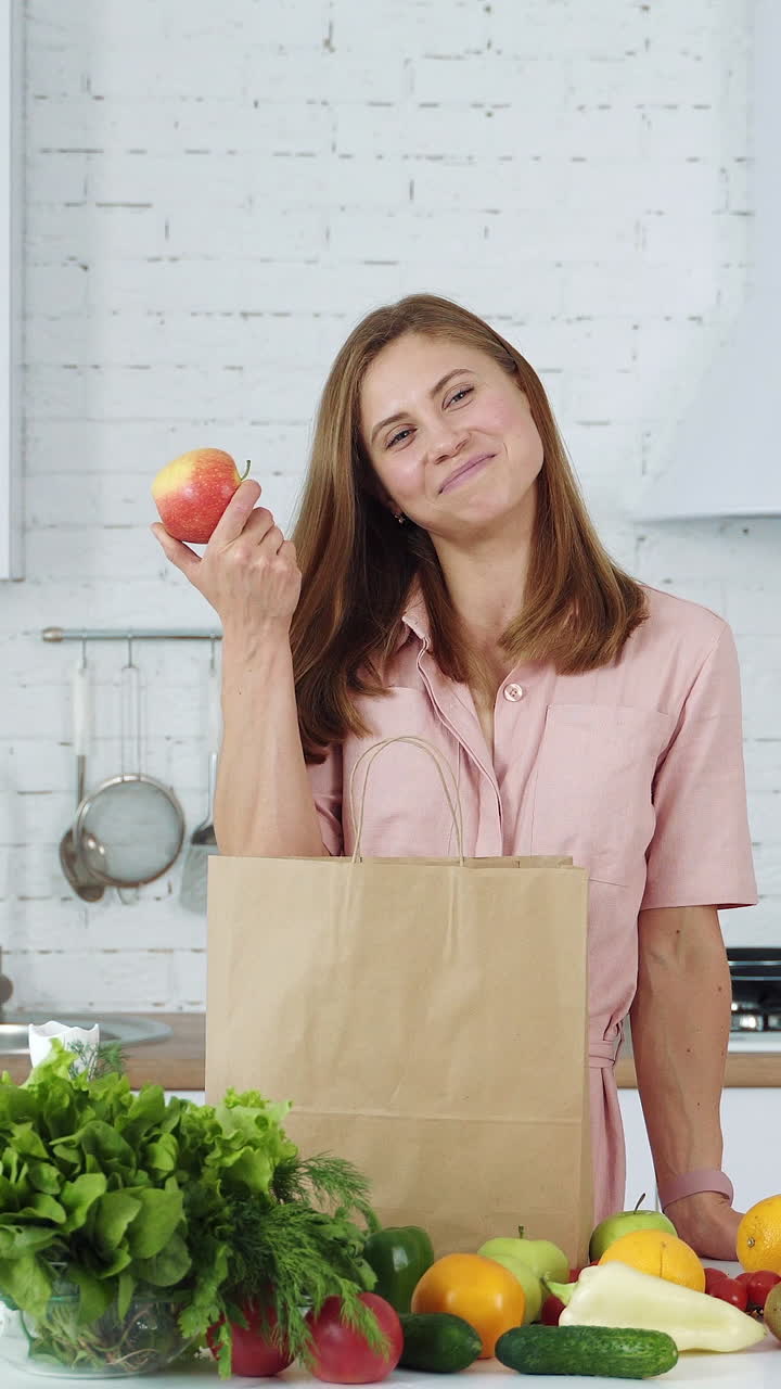 Woman unpacks vegetables and fruits from a supermarket bag. Girl at home in a white kitchen. Vertical video