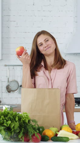 woman unpacks vegetables and fruits from a supermarket bag. girl at home in a white kitchen. vertical video