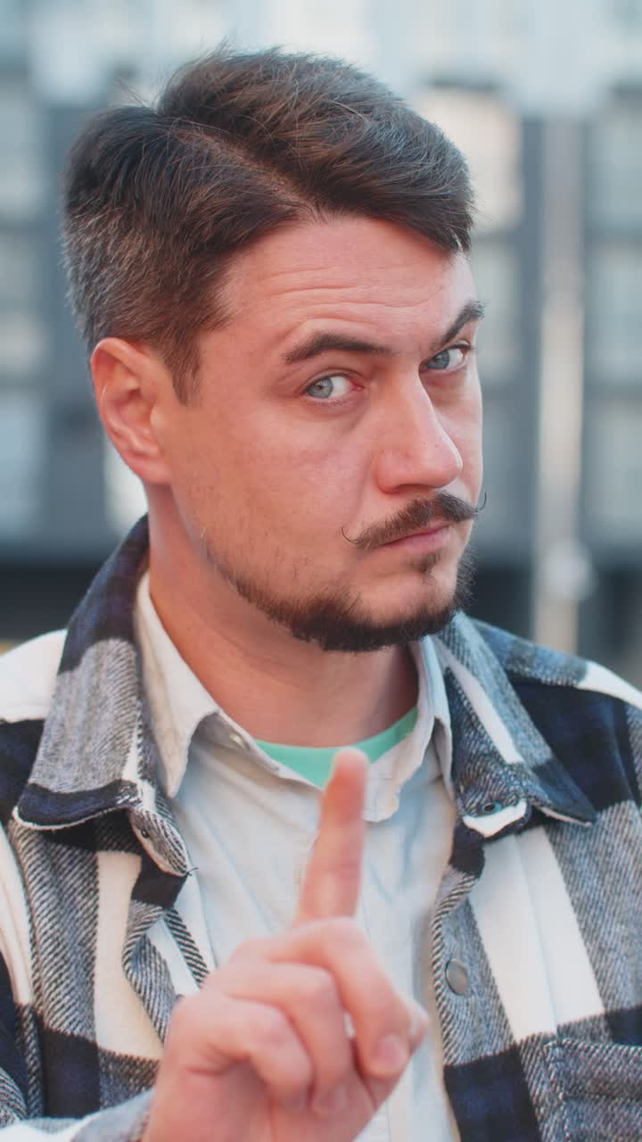 백인 남자가 입술에 지표손가락을 러 침을 만들고 시내 거리에서 시끄러운 몸짓을 합니다.