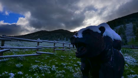 time lapse of a statue of a bear. snow is lightly dusted on top of it with a green meadow surrounding it. (slow motion)