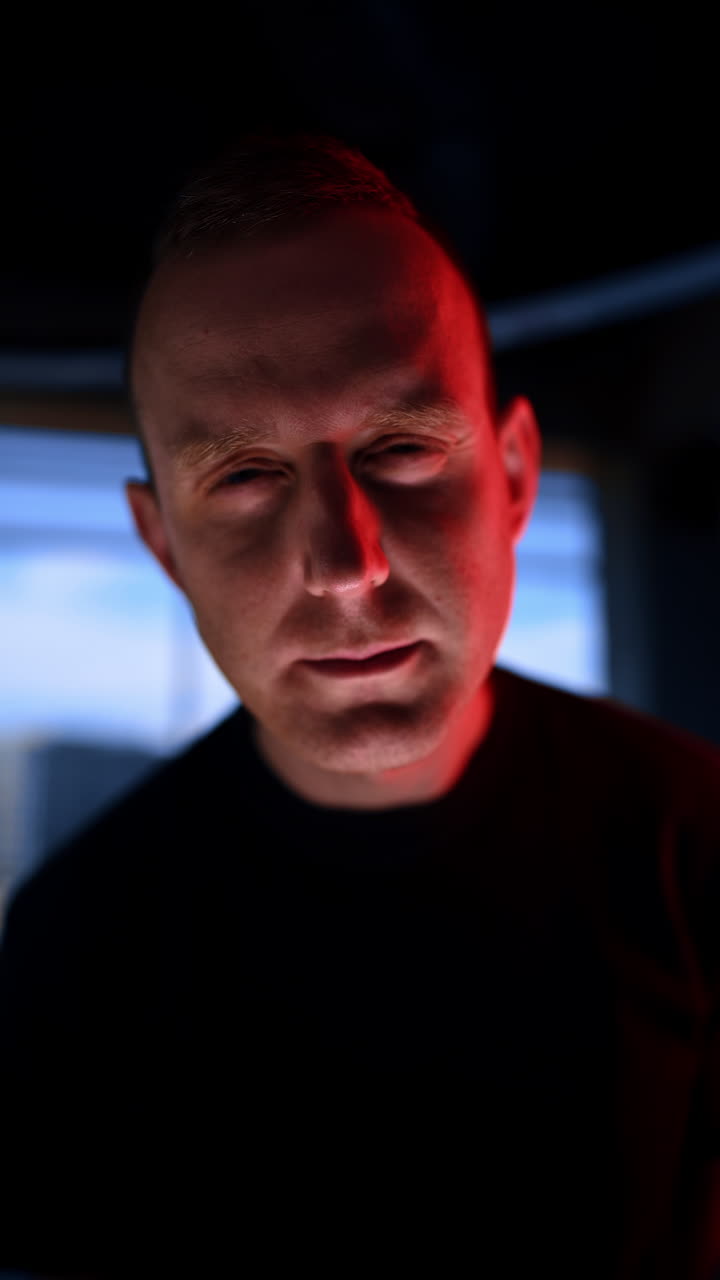Mid-aged Caucasian man wearing black t-shirt stands in front of camera. Man in the room with flashing light tilting head from side to side. Close up. Vertical video.