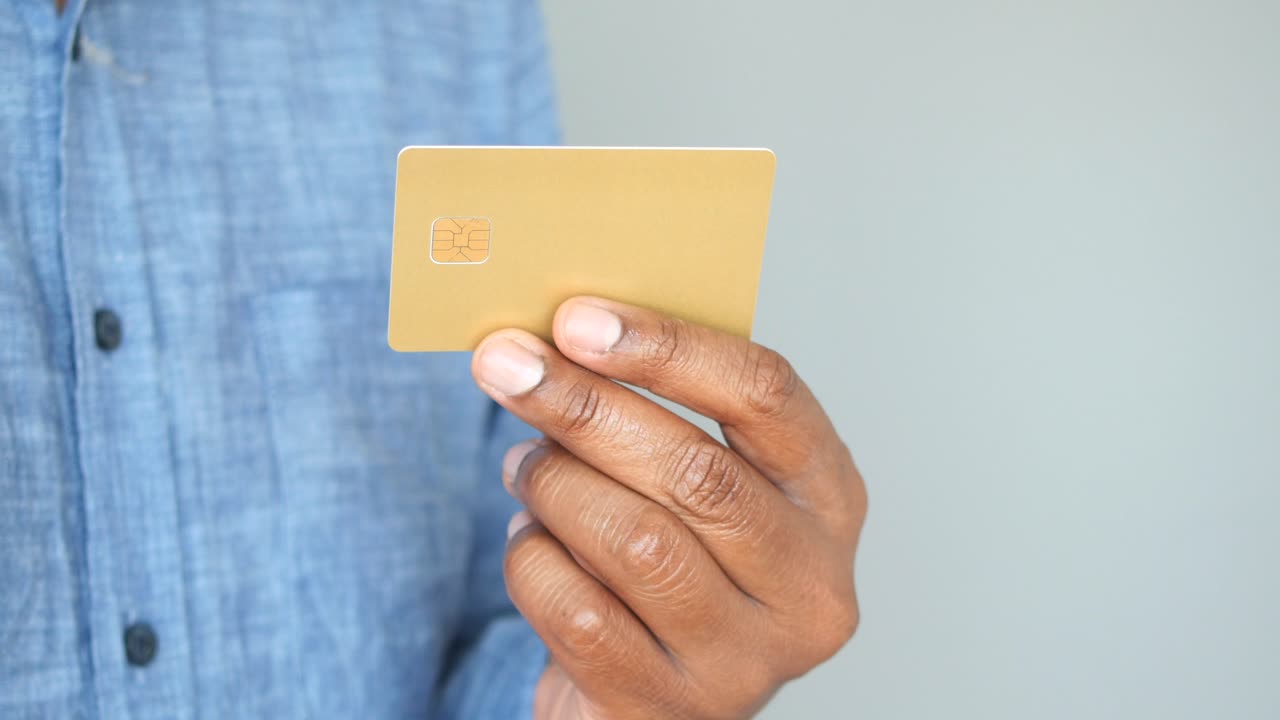 A mão de um homem segurando um cartão de crédito dourado
