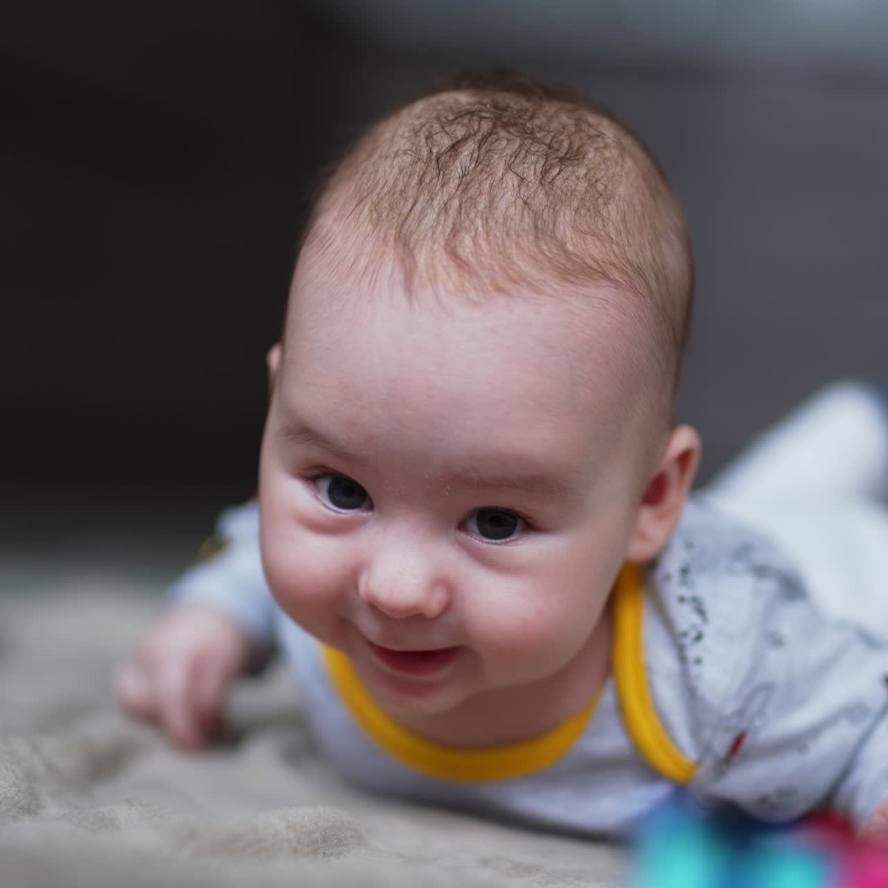 Cute adorable baby boy lies on tummy looking aside. Lovely beautiful kid smiling sweetly to something. Close up