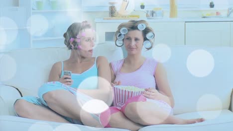 animation of light spots over caucasian female friends eating popcorn and talking