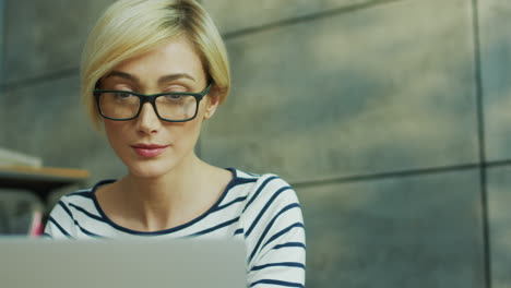 Close-Up-Of-The-Young-Blond-Attractive-Businesswoman-In-Glasses-Sittingat-The-Laptop-Computer-Screen-In-The-Loft-Office-Room