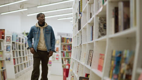 young man exploring bookshelf in modern bookstore, walking down aisle between white shelves filled with various books. stylish interior with warm lighting creates inviting atmosphere