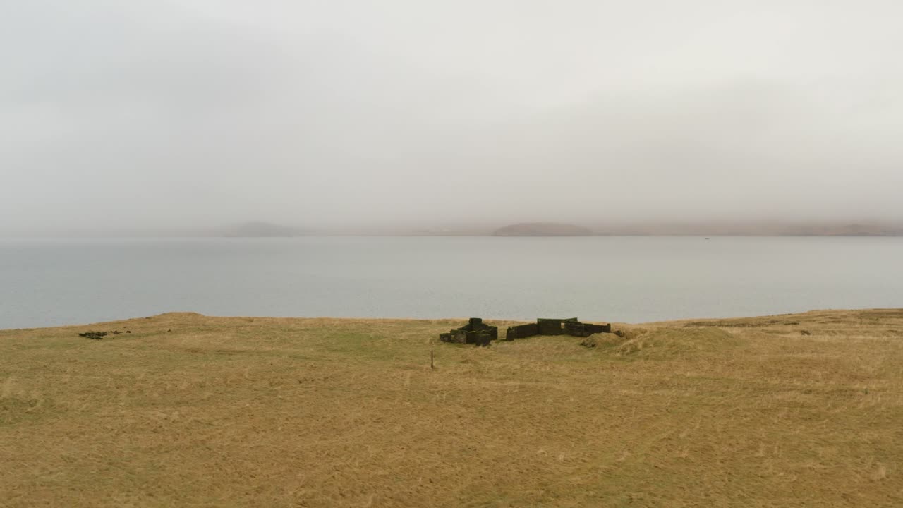 Rovine di fondamenta in pietra su una nebbiosa collina costiera a Hvalfjörður, in Islanda, con vista su un tranquillo fiordo
