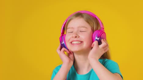studio shot of girl wearing headphones listening to music against yellow studio background - shot in slow motion