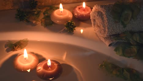 relaxing spa background with candles floating in the bath water, some green petals and a towel near the water surface