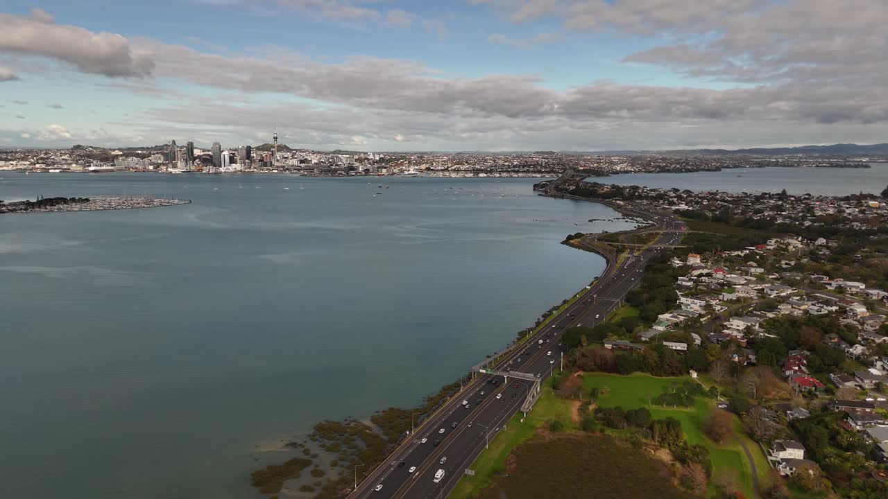 A dynamic 4K 60fps drone reveal, flying backward over motorway traffic near Shoal Bay to showcase Auckland's iconic CBD skyline. Captures the city's commute, infrastructure, and landscape in one shot