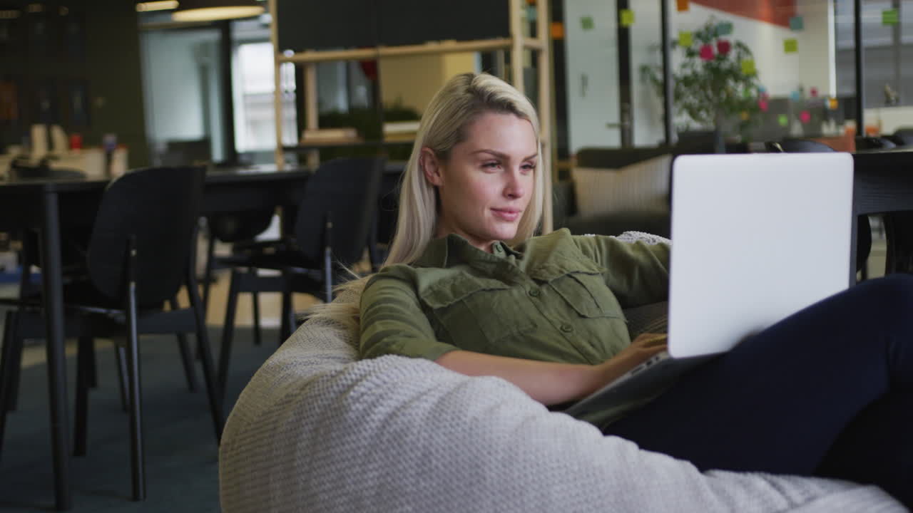 Caucasian businesswoman sitting on pouf using a laptop in modern office