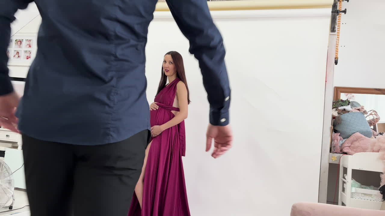 Pregnant woman and partner pose during a photo shoot in a studio setting with a white backdrop