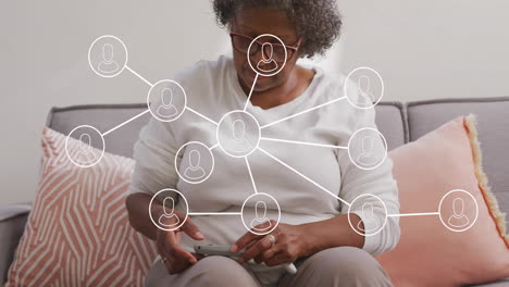Senior woman using smartphone in living room, displaying digital network connection icons overhead