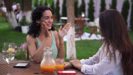 two women talking at the cafe: brunette girl emotionally sharing her engagement and showing the ring