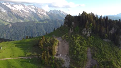 Drohnenaufnahme-Eines-Schroffen,-Mit-Kiefern-Bewachsenen-Berges,-Der-Im-Hintergrund-Eine-Schneebedeckte-Und-Felsige-Bergkette-Zeigt