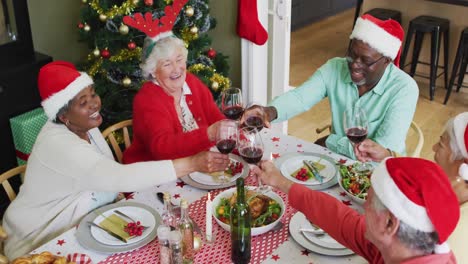 Fröhliche-Gruppe-Verschiedener-älterer-Freunde,-Die-Zur-Weihnachtszeit-Essen-Feiern-Und-Wein-Trinken
