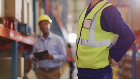 Diverse-male-workers-wearing-helmet-and-touching-back-in-warehouse