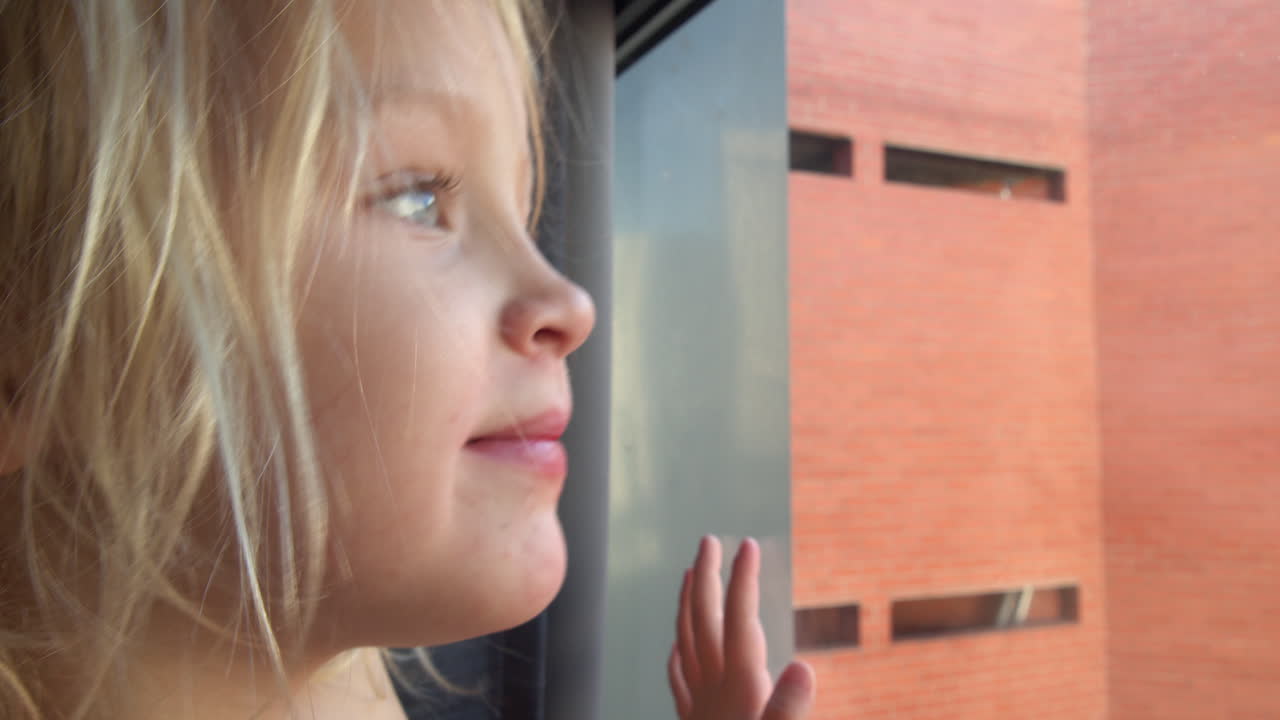 Cheerful and curious little girl looking outside through the window