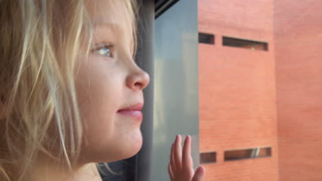 cheerful and curious little girl looking outside through the window