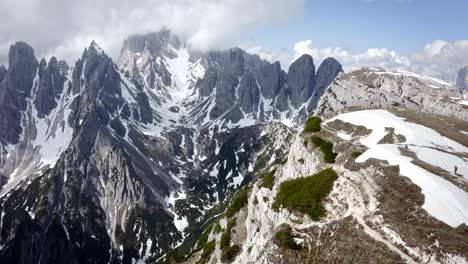 hikers atop a sharp rocky mountain ridge rising above a green valley with snow