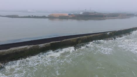 Luftaufnahme-Des-Holzterminalkrans,-Der-Holz-In-Das-Frachtschiff-Verlädt,-Hafen-Von-Liepaja,-Holzholzexport,-Bewölkter-Tag-Mit-Nebel-Und-Dunst,-Hackschnitzelhaufen,-Drohne-Bewegt-Sich-Vorwärts