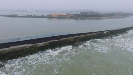 vista aérea de establecimiento de grúa terminal de madera cargando madera en el buque de carga, puerto de liepaja, exportación de troncos de madera, día nublado con niebla y niebla, pilas de astillas de madera, drones avanzando