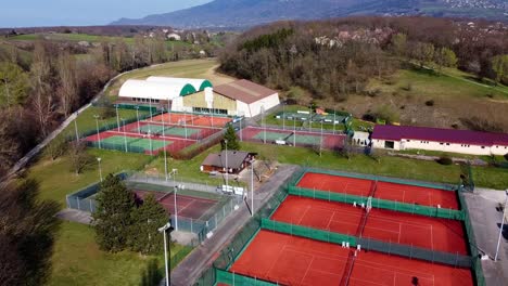 Drohnenaufnahme-Leerer-Tennisplätze-Während-Der-Sperrung-Mit-Einem-Wald-Und-Einem-Park-Dahinter