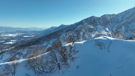 Toma-Aérea-Empujando-Sobre-La-Cima-De-La-Montaña-Myoko,-La-Cámara-Se-Desplaza-Hacia-Abajo-Revelando-La-Altura-Y-Escala-De-La-Montaña