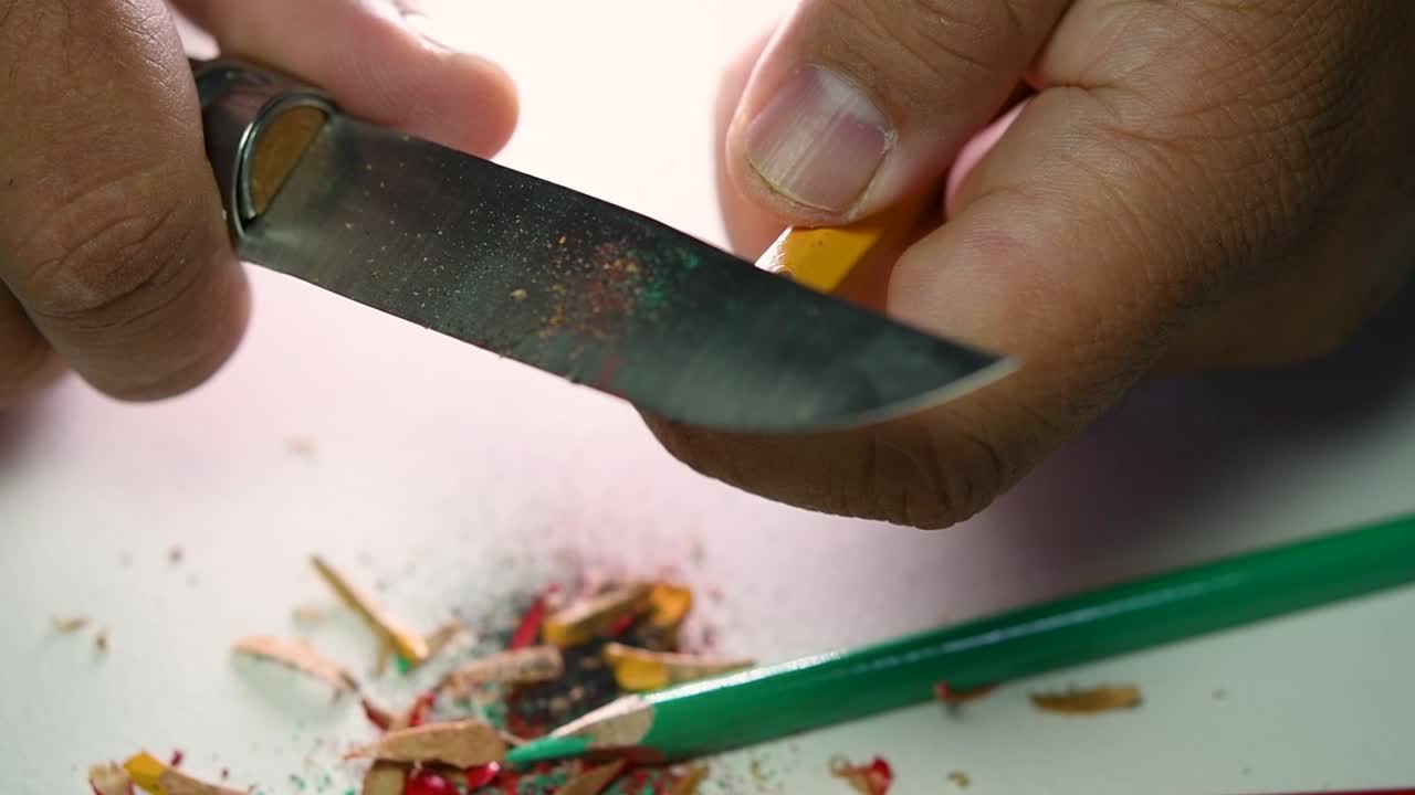 Opptak av hender som sakte spisser en blyant og noen fargeblyanter med en skarp kniv