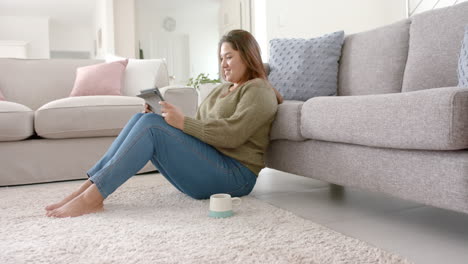 happy plus size biracial woman relaxing in living room using tablet, copy space, slow motion