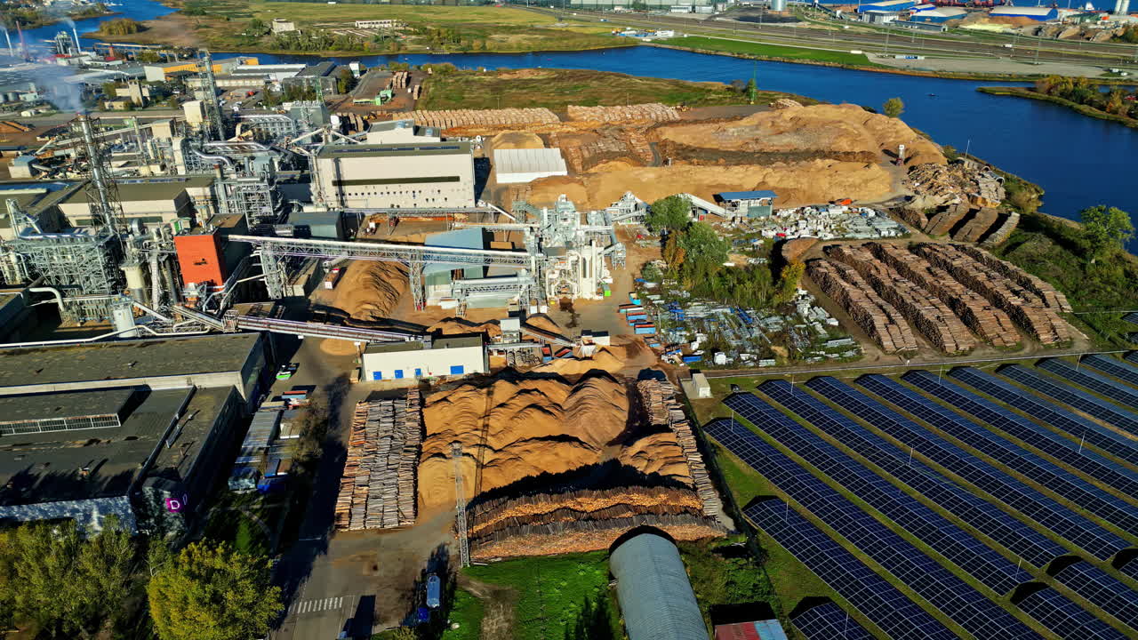 Aerial view of a Latvian wood factory with logs, woodchips, and solar panels nearby