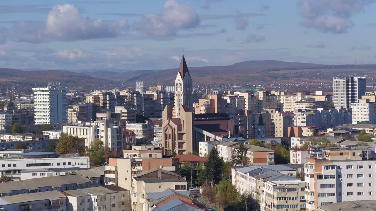 A slow-panning aerial shot of Bacau, Romania, focusing on the church, which is surrounded by dense residential apartment blocks on a sunny day