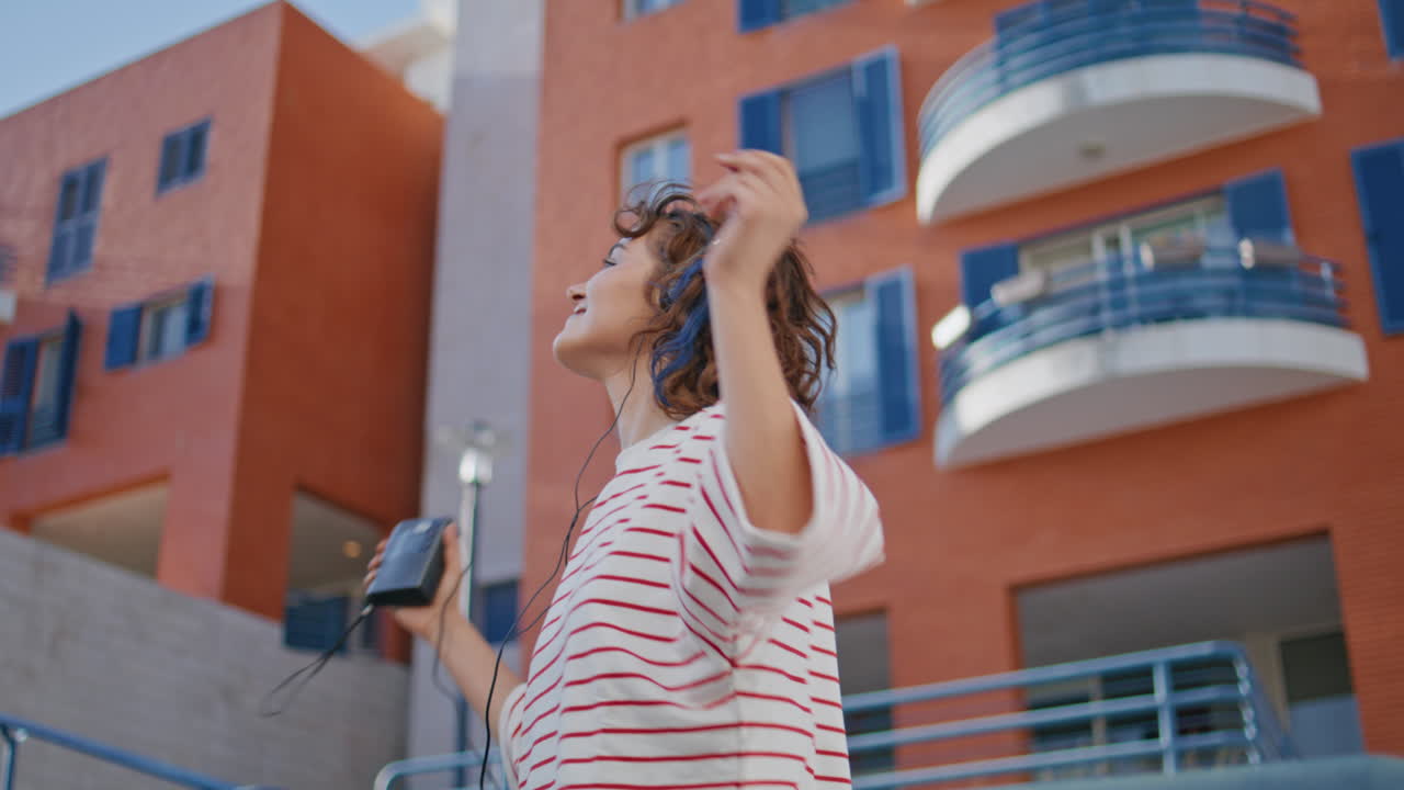 길거리에서 헤드폰으로 춤을 추는 소녀 멜로마니아 여성이 음악을 듣고 있습니다.