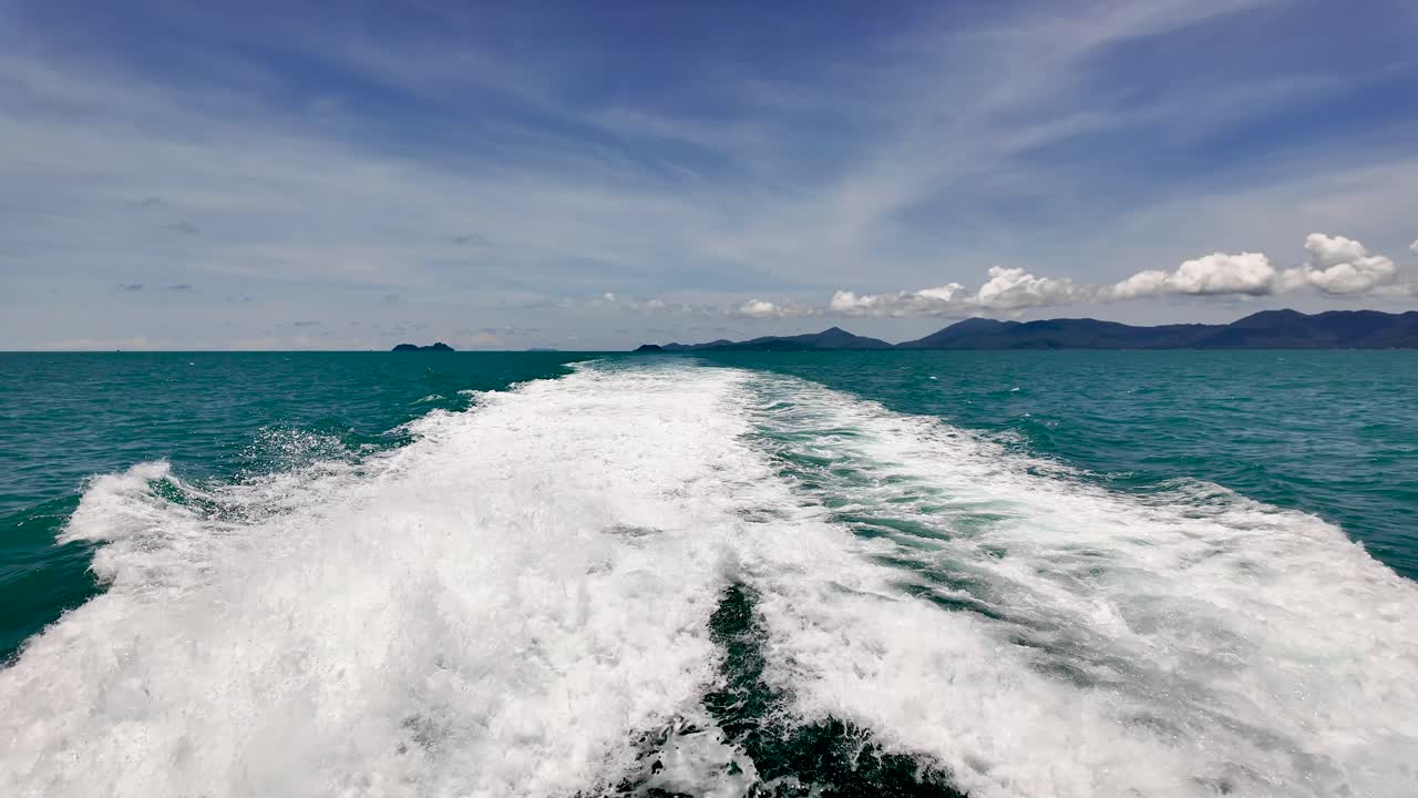 An exhilarating view of ocean waves trailing a fast-moving ferry in Thailand, set against the serene backdrop of a clear blue sky. slow motion