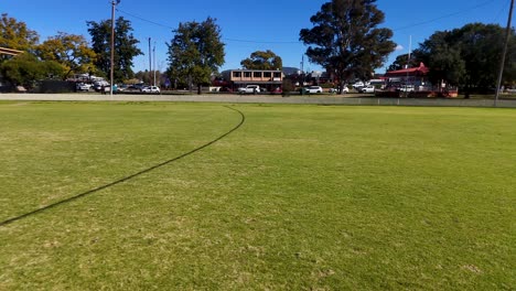 wide-angle camera pans across an empty sports ground with green grass, soccer goalposts, and clear blue sky, capturing midday natural lighting and open space