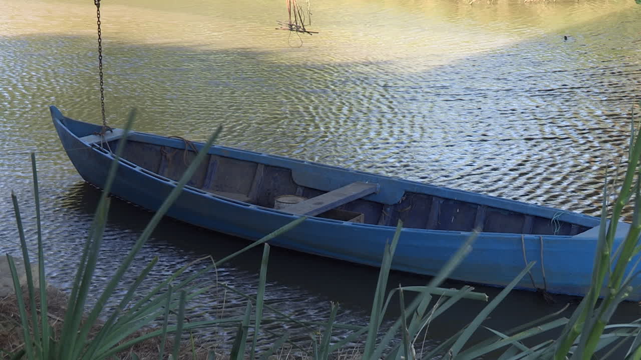 un barco de pesca artesanal, de madera y pintado de azul, se mueve lentamente en las tranquilas aguas del río