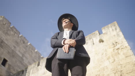 low angle view of a man in black suit and hat looking around beside a castle in jerusalem on a sunny day