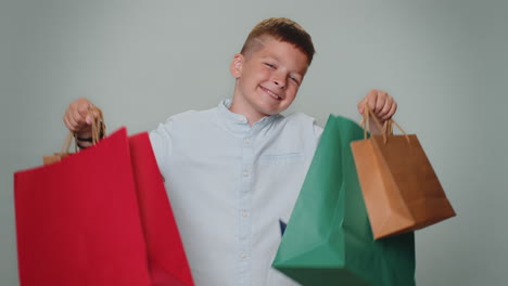 Toddler-boy-showing-shopping-bags,-advertising-discounts,-smiling-looking-amazed-with-low-prices