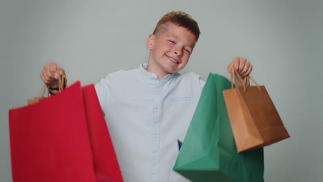 niño pequeño mostrando bolsas de compras, descuentos publicitarios, sonriendo mirando asombrado con los precios bajos