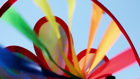 colored rainbow spinning pinwheel toy in the wind against blue sky landscape. alternative energy