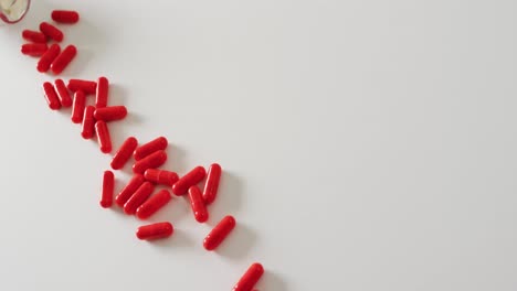 Video-of-white-pill-box-spilling-red-pills-on-white-background-with-copy-space