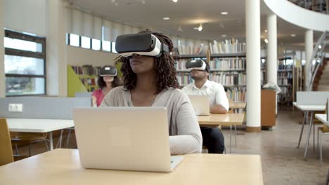 Front-view-of-young-woman-with-VR-glasses-sitting-at-library