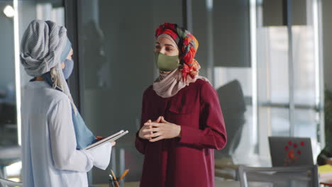 Two-Muslim-Businesswomen-in-Masks-Talking-in-Office