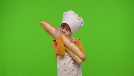 Child-girl-kid-dressed-as-cook-chef-showing-sniffing-two-fresh-baguettes,-stretches-bread-to-camera