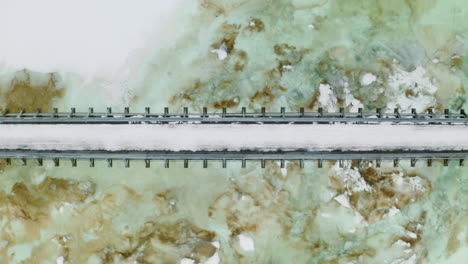 person walking in narrow bridge over a frozen river in norway in winter - aerial shot